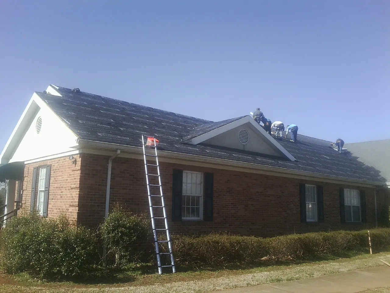 Crew tearing shingles off a brick ranch roof with a ladder set — Emergency Roof Repair work by our crew in Line Lexington