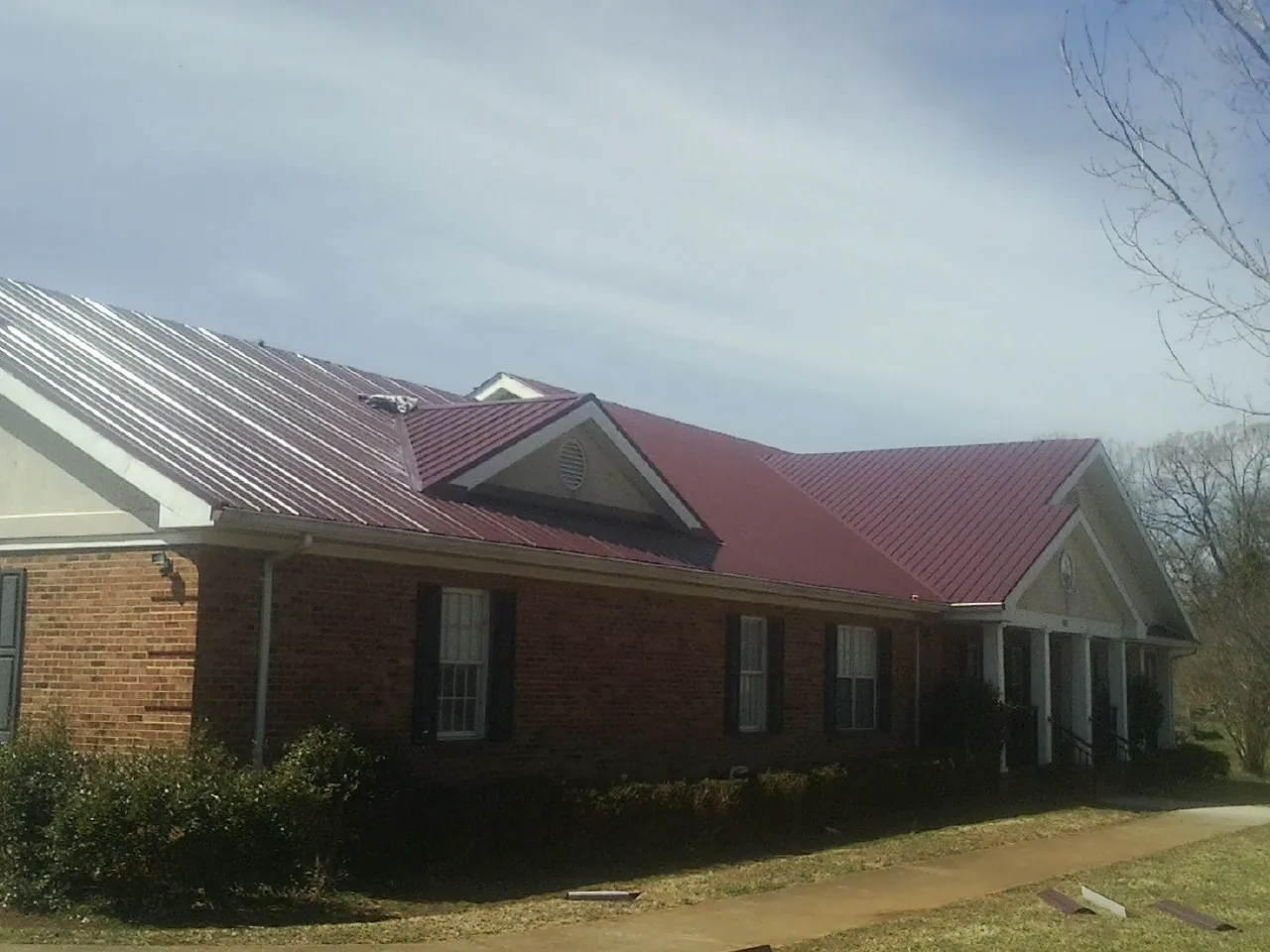 Red metal roof with gabled entries on a long brick building, from a Hail Damage Roof Repair job in Line Lexington
