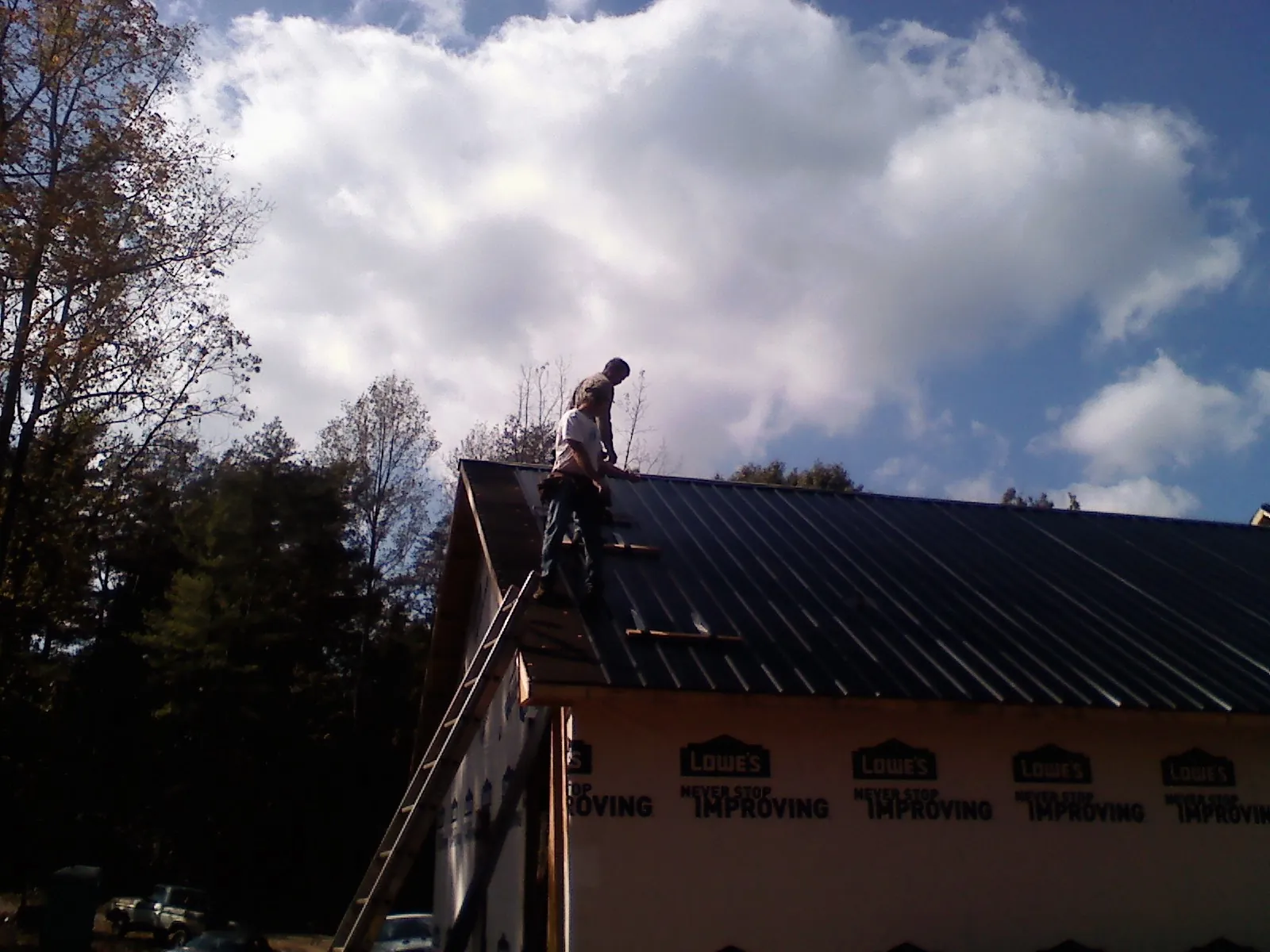 Roofer fastening dark metal panels high against a cloudy sky, from a Roof Inspection job in Line Lexington