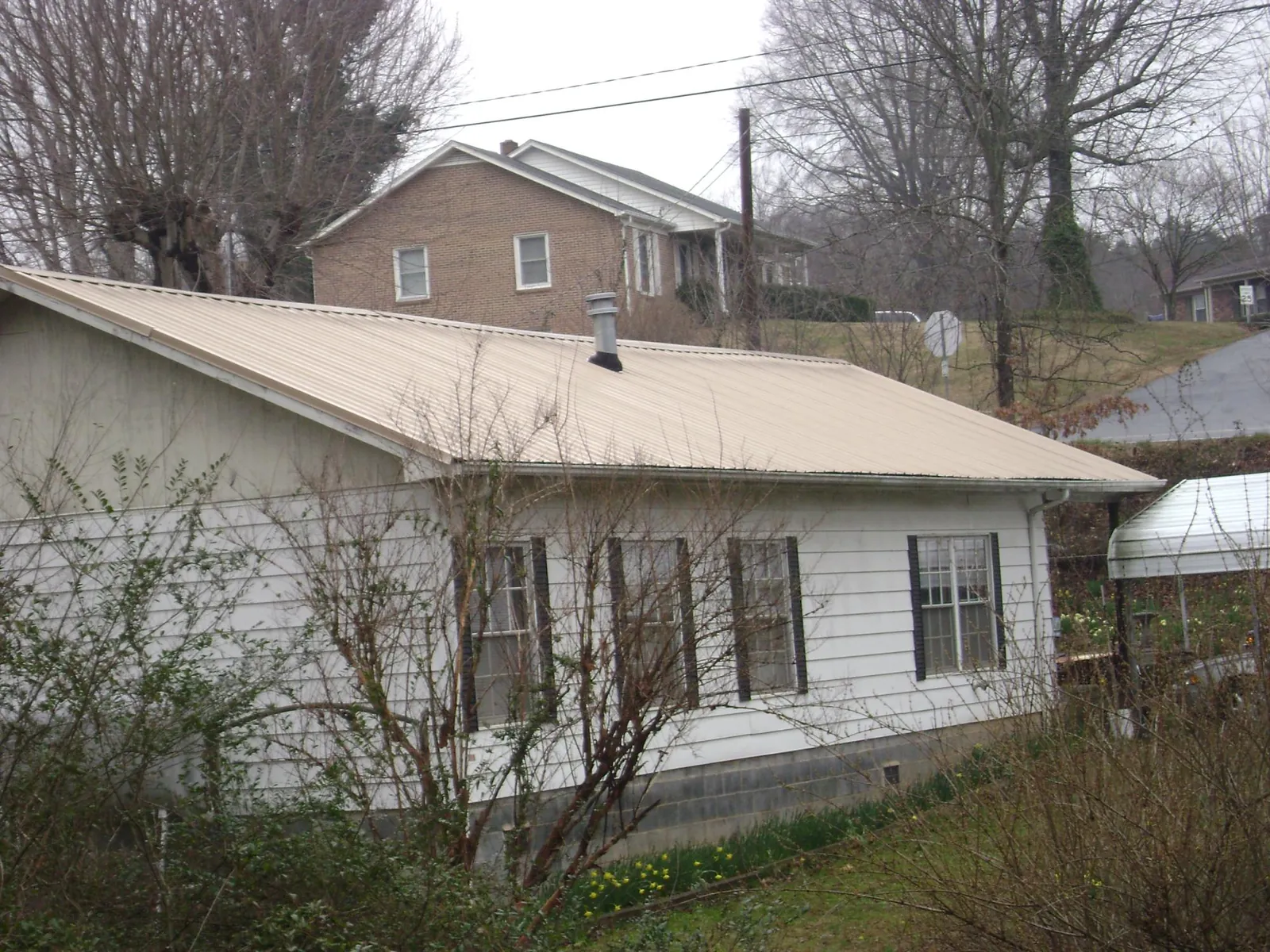 Tan metal roof on a white sided house set into a hillside — Commercial Roofing by Roofing Brothers in Line Lexington