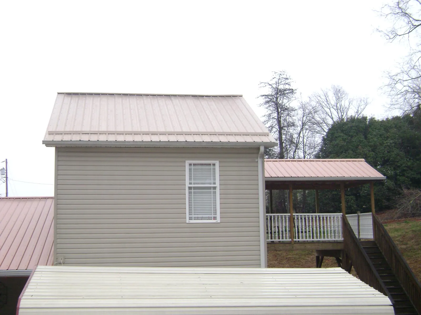 Tan metal roofs on a two story addition and attached porch, from a Roof Replacement job in Line Lexington